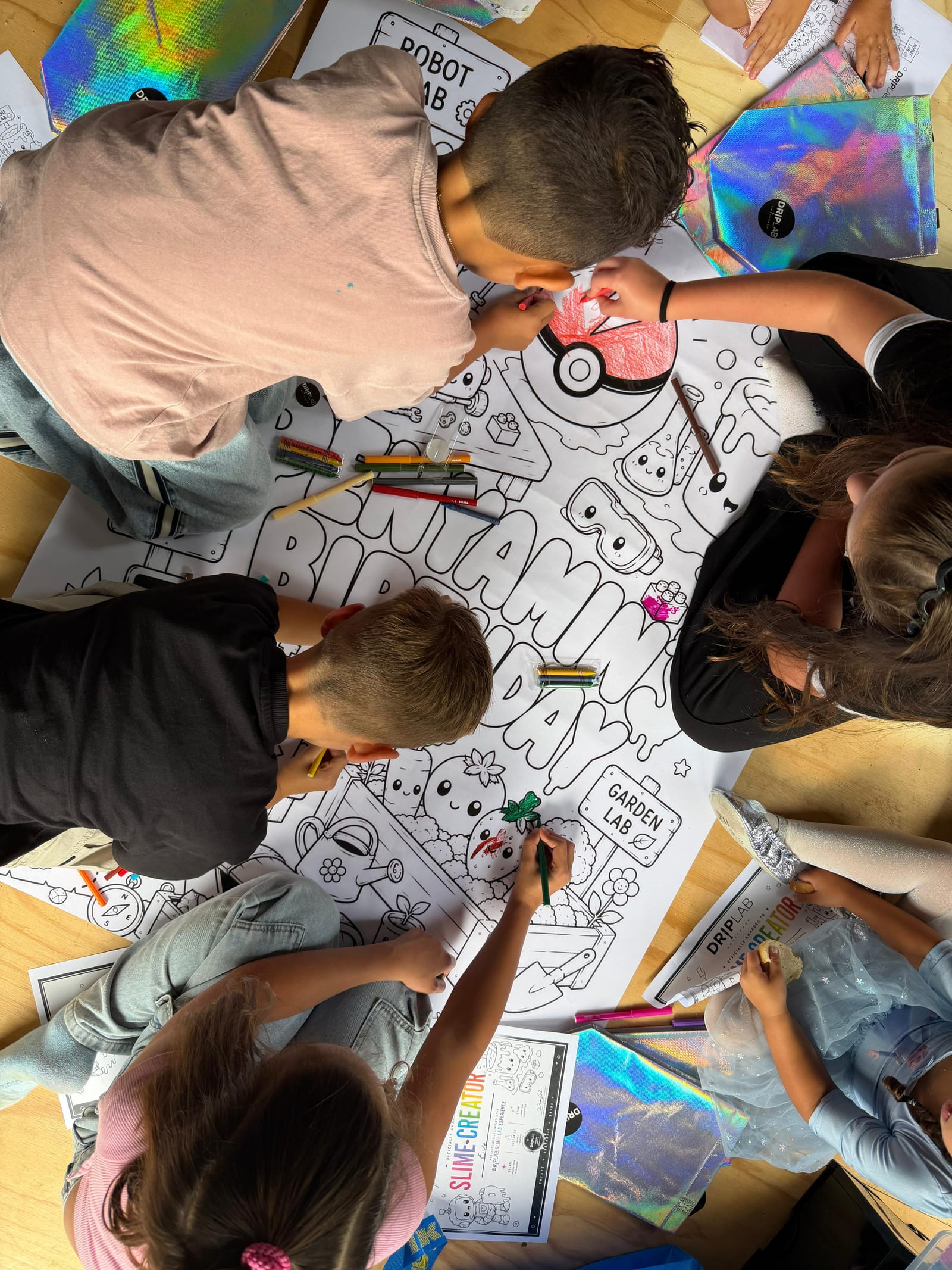 Groep kinderen werkt samen aan een grote kleurplaat op tafel
