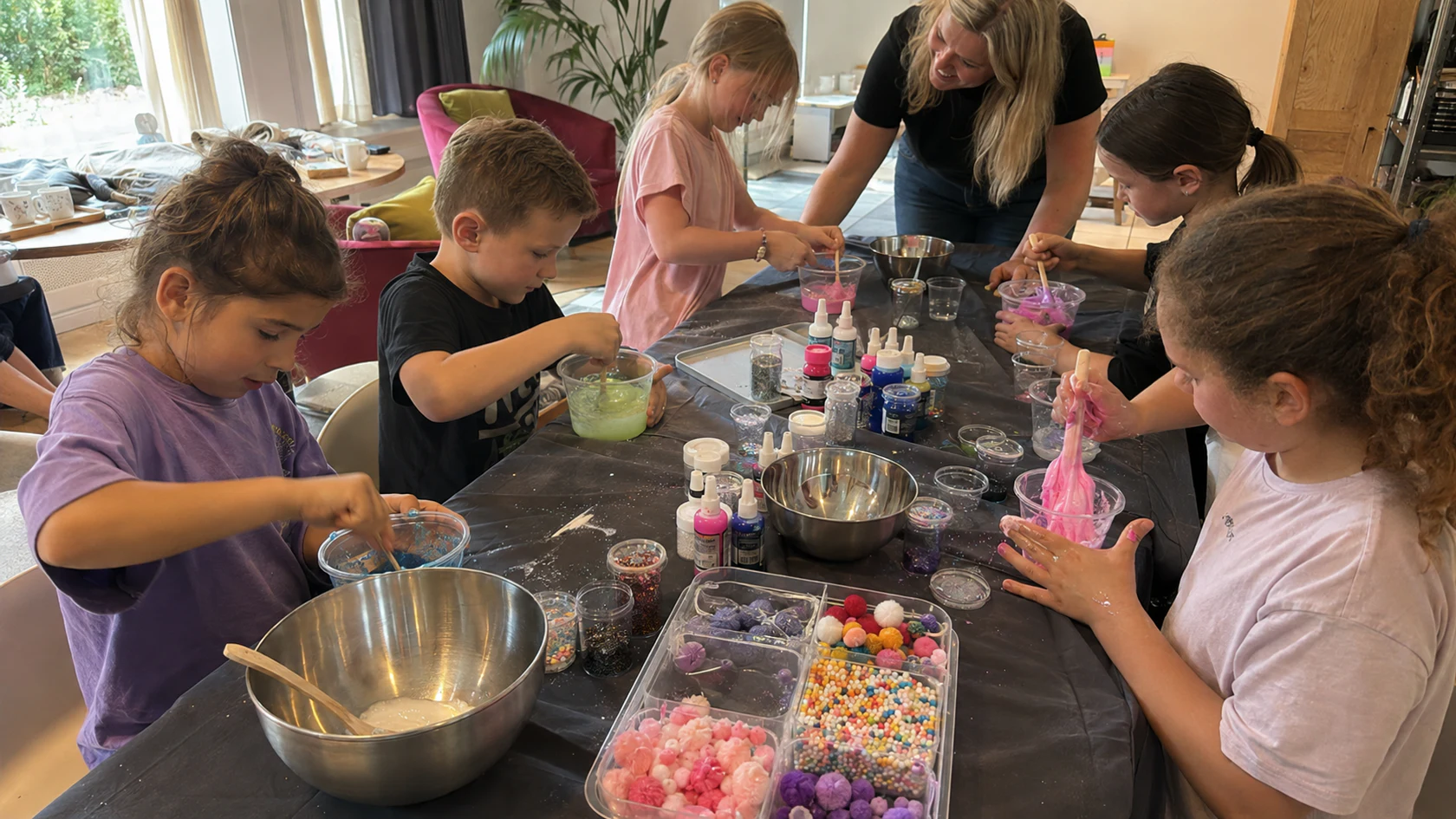 Kinderen maken samen slijm aan een volle werktafel terwijl een begeleider helpt